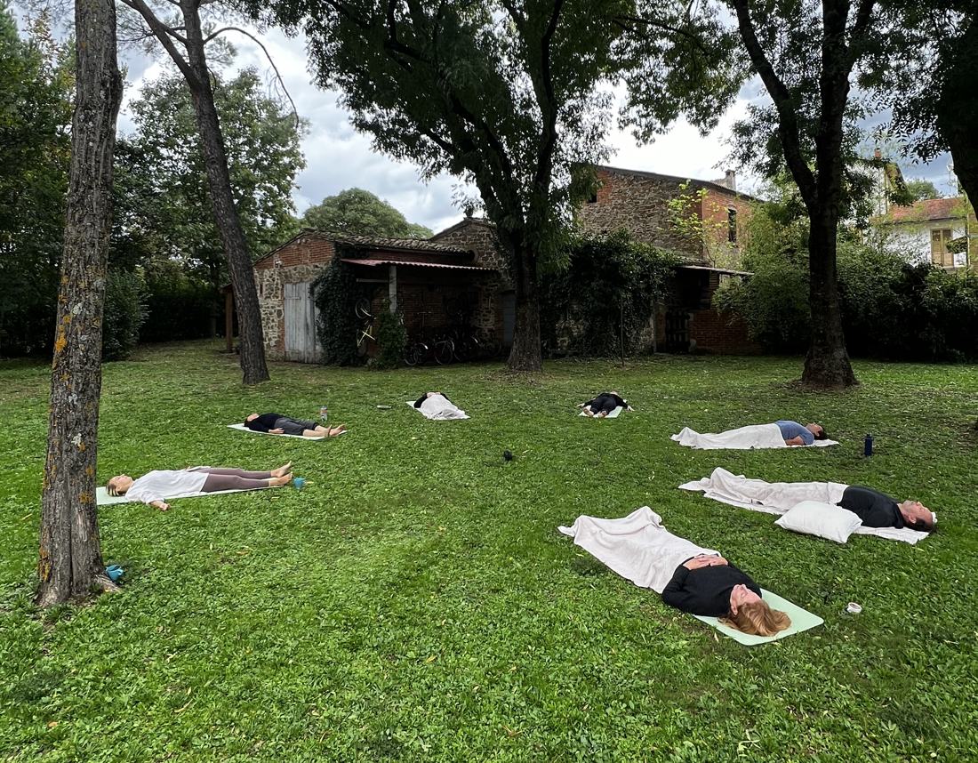 The group resting in savasana on the lawn beneath the trees
